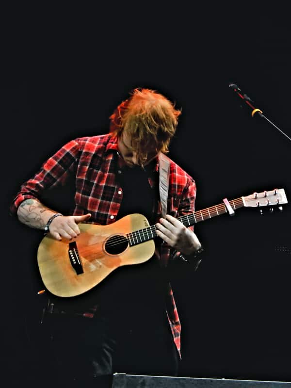 Ed Sheeran playing guitar on stage with a capo